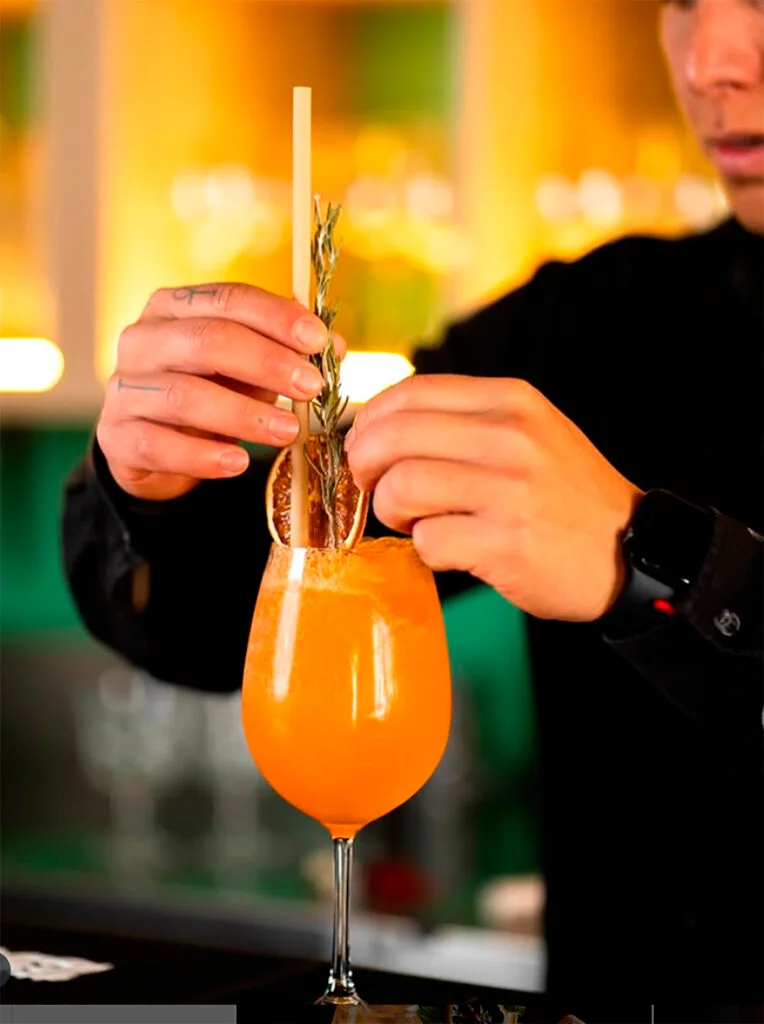 “Coctelero de La Guarida de Palma decorando un cóctel naranja con cítrico y romero.”