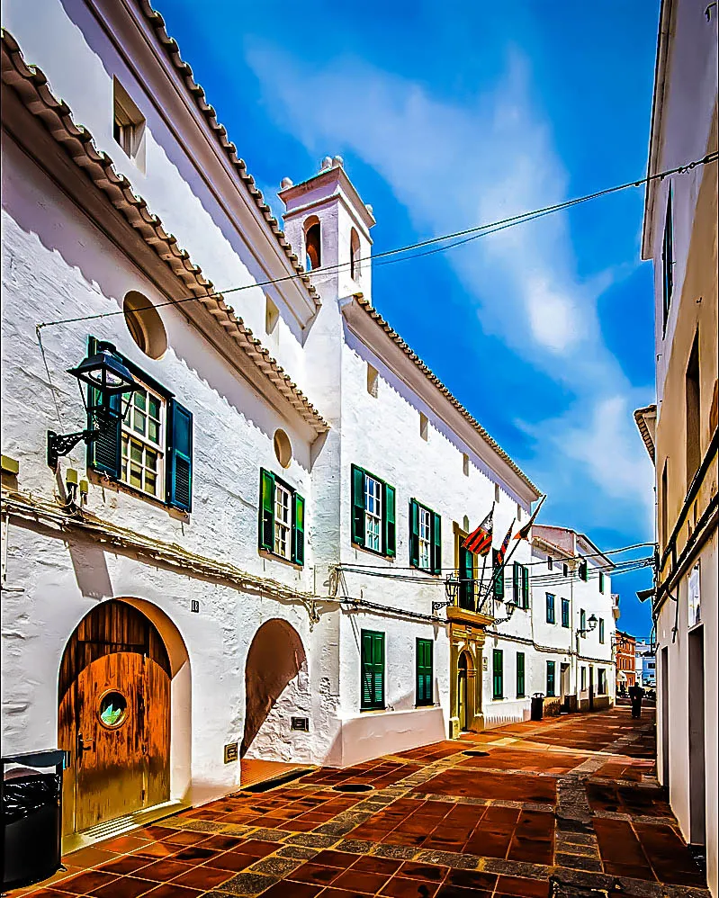 Calle tradicional en Es Mercadal, Menorca, con arquitectura blanca, detalles verdes y atmósfera mediterránea