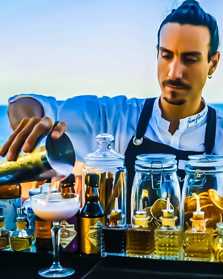Bartender preparando cóctel en The Sky Cocktail Bar Formentera con ingredientes artesanales y fondo costero