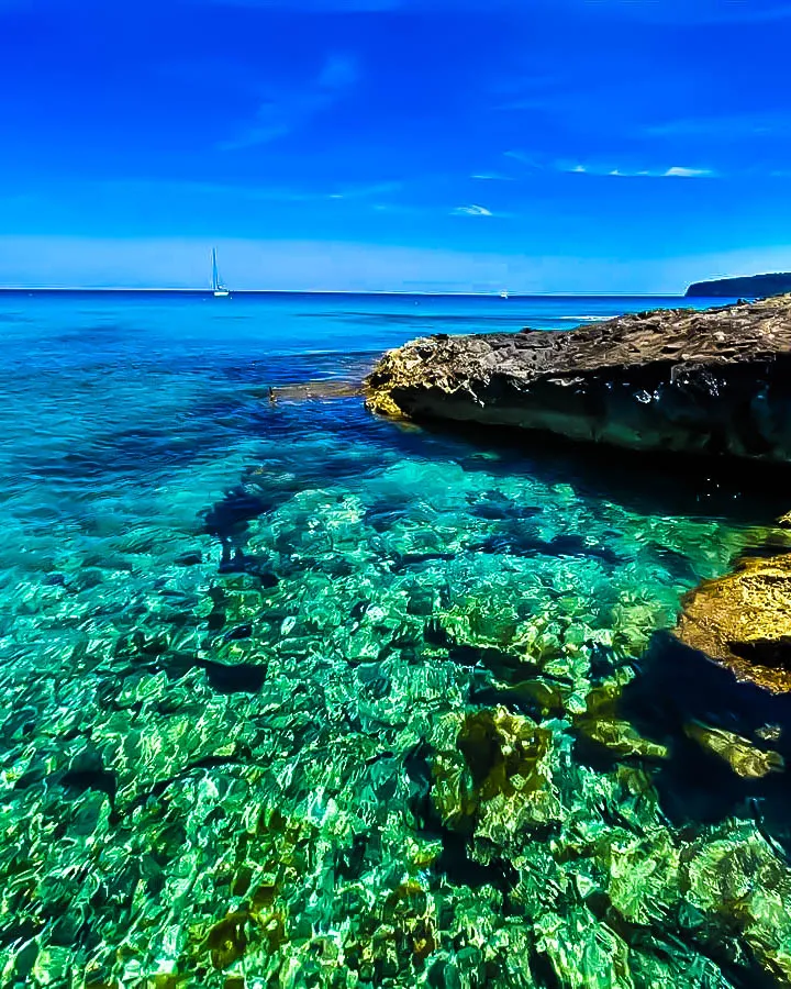 Costa rocosa de Formentera con aguas turquesa y velero en el horizonte
