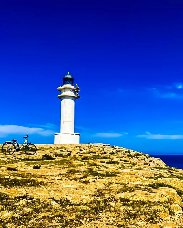 Faro blanco en Formentera con bicicleta aparcada sobre terreno rocoso y cielo azul intenso