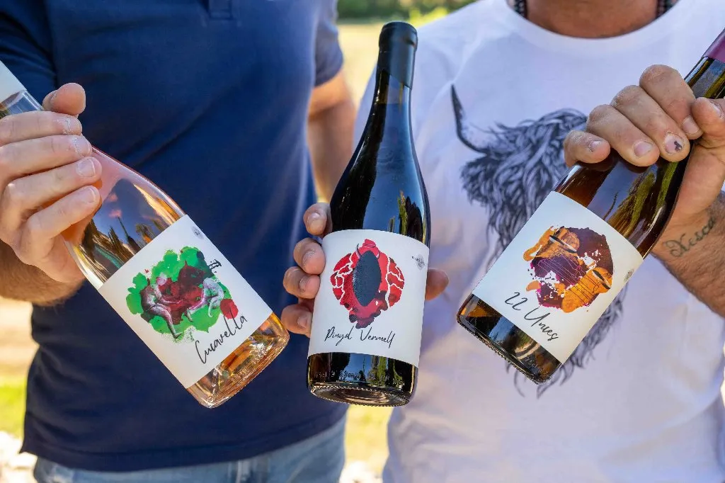 Dos personas mostrando tres botellas de vino artesano: Cuarella, Brutal Vernell y 22 Uvas